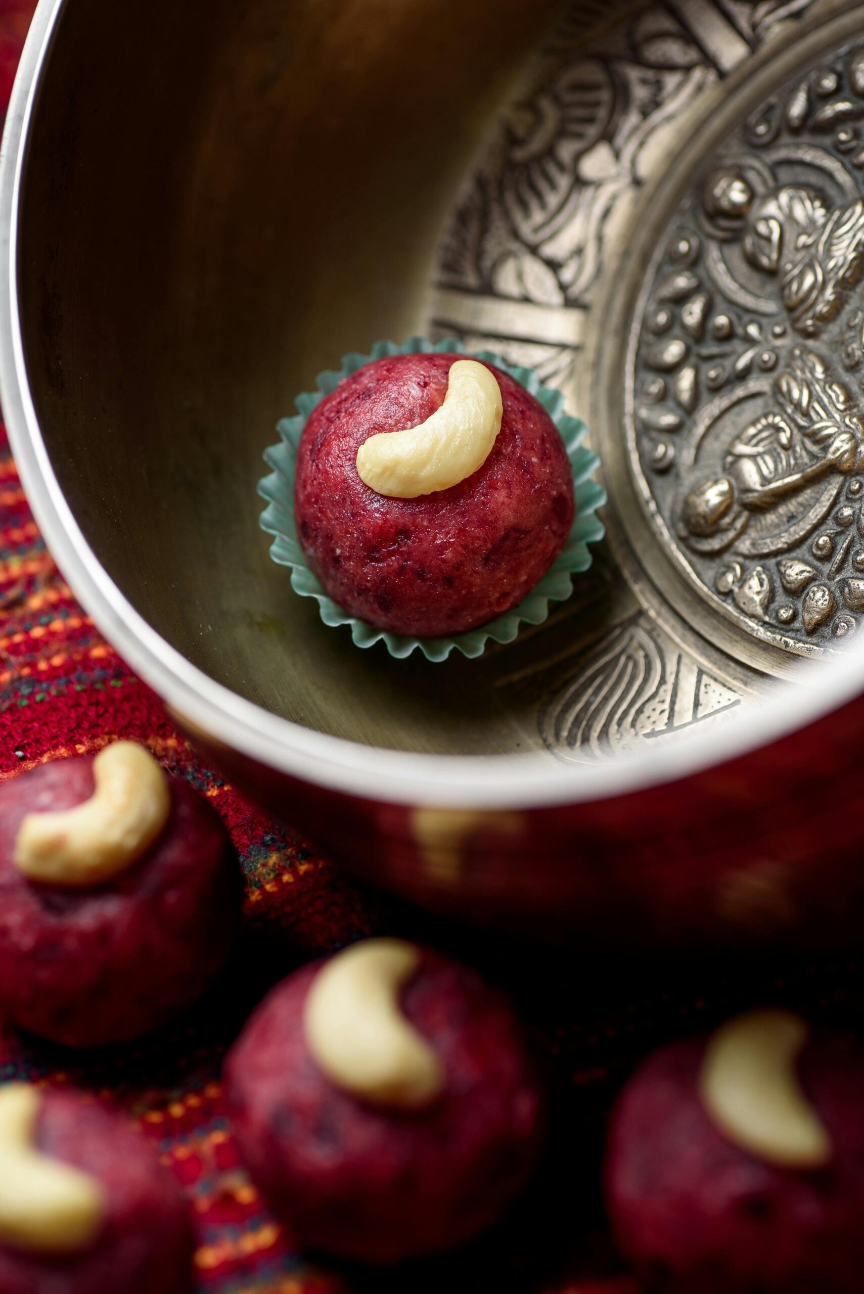 Vegan red ladoo with cashew on top, presented in an ornate bowl, showcasing traditional Indian dessert style.
